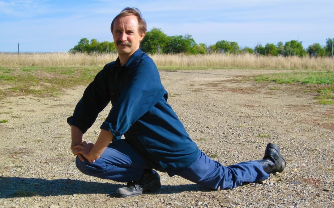 Paulie Zink doing advanced Yin yoga pose in leather work boots on rocky ground