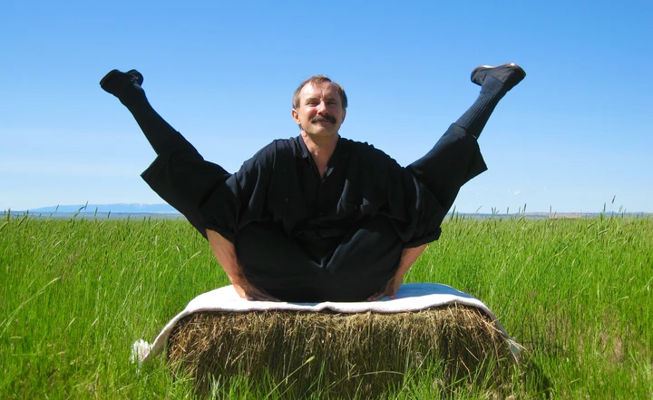 Yin Yoga Founder Paulie Zink Yin yoga founder Paulie Zink balancing on his hands with legs raised, on a hay bale in a grassy field